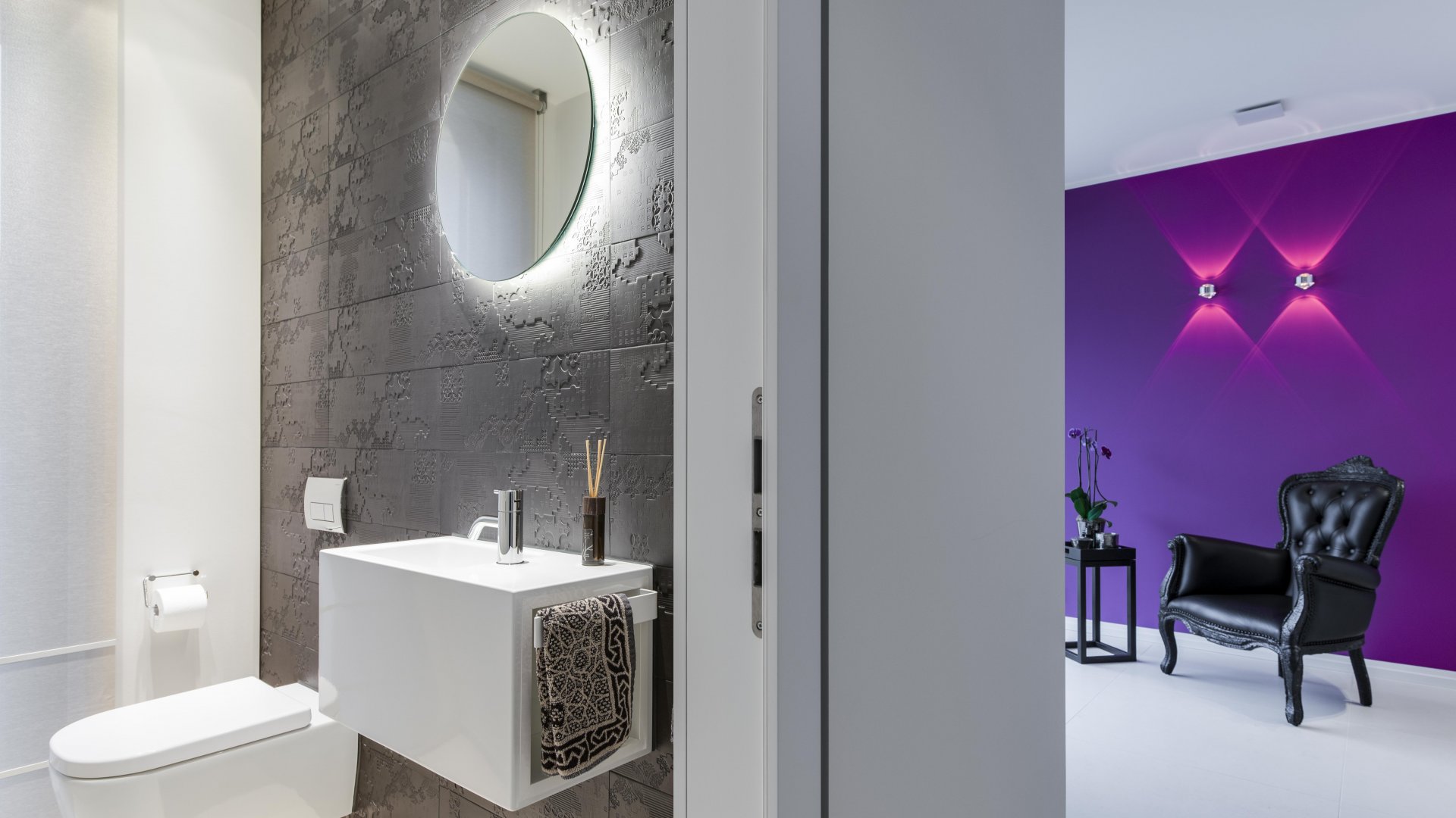 Schwarz-weißes Gäste-WC mit farbigem Flur, Wandspiegel run hinterbeleuchtet, indirektes Licht, Handtuchhalter