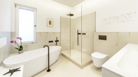 Freistehende Badewanne aus Corian, mattweiß, Sitzbank mit Auszug, gespachtelter Boden im Beton-Look fugenlos, Duschabtrennung rahmenlos, Armaturen in Exklusivfarbe Messing gebürstet, Namasté,